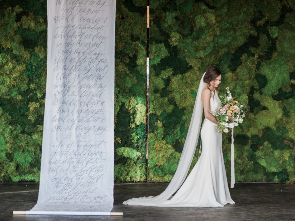 bride holding bouquet in front of moss wall with hand scripted scroll at Moss | Denver