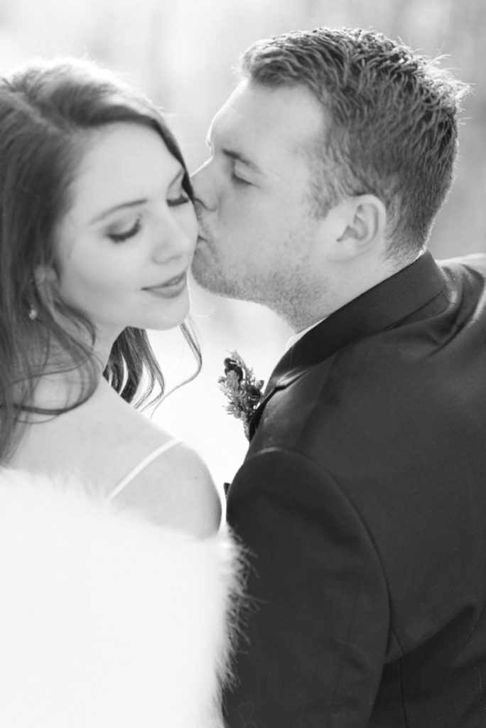 groom kisses bride on the cheek during intimate wedding in black and white image