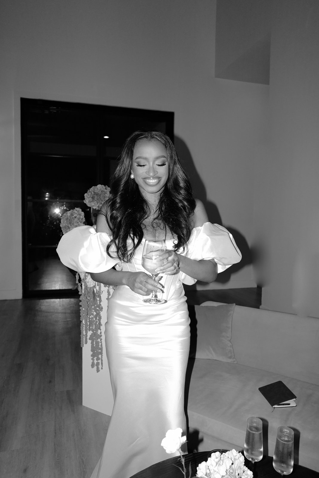 bride in a black and white image holding a glass of champagne celebrating her wedding weekend